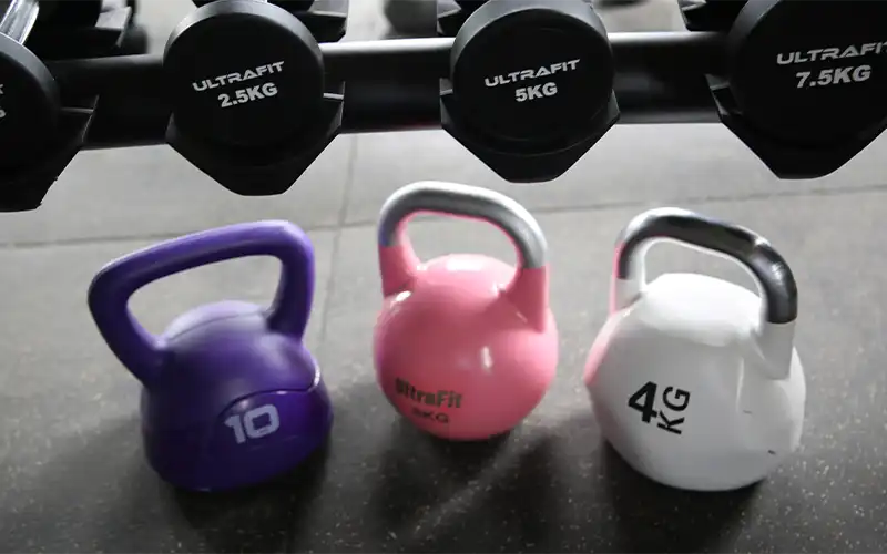 Variety of rubber hex dumbbells and rubber kettlebells on display rack showing different weights and sizes