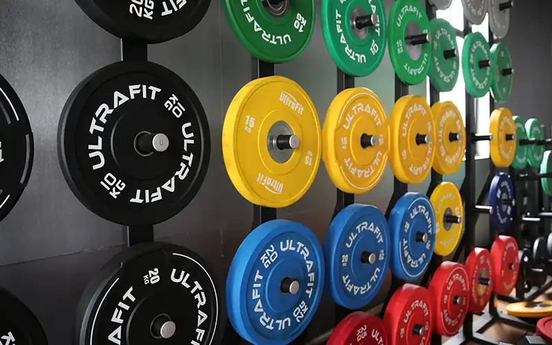Weight plate storage rack with rubber-coated plates organized by size, showing proper gym organization